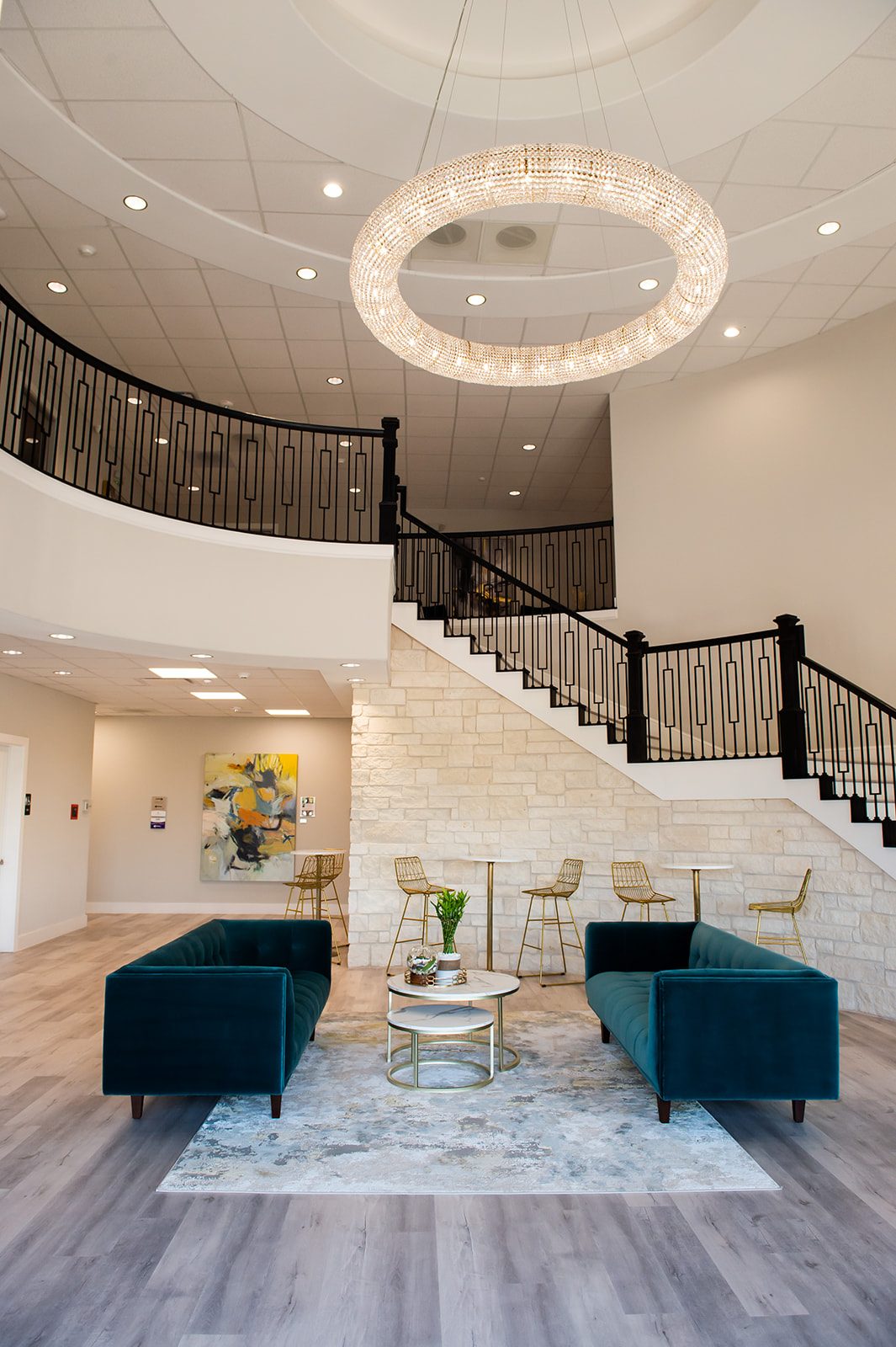 Crystal ring chandelier above the Bellevana lobby, curved balcony, staircase, and stone wall with teal sofas below