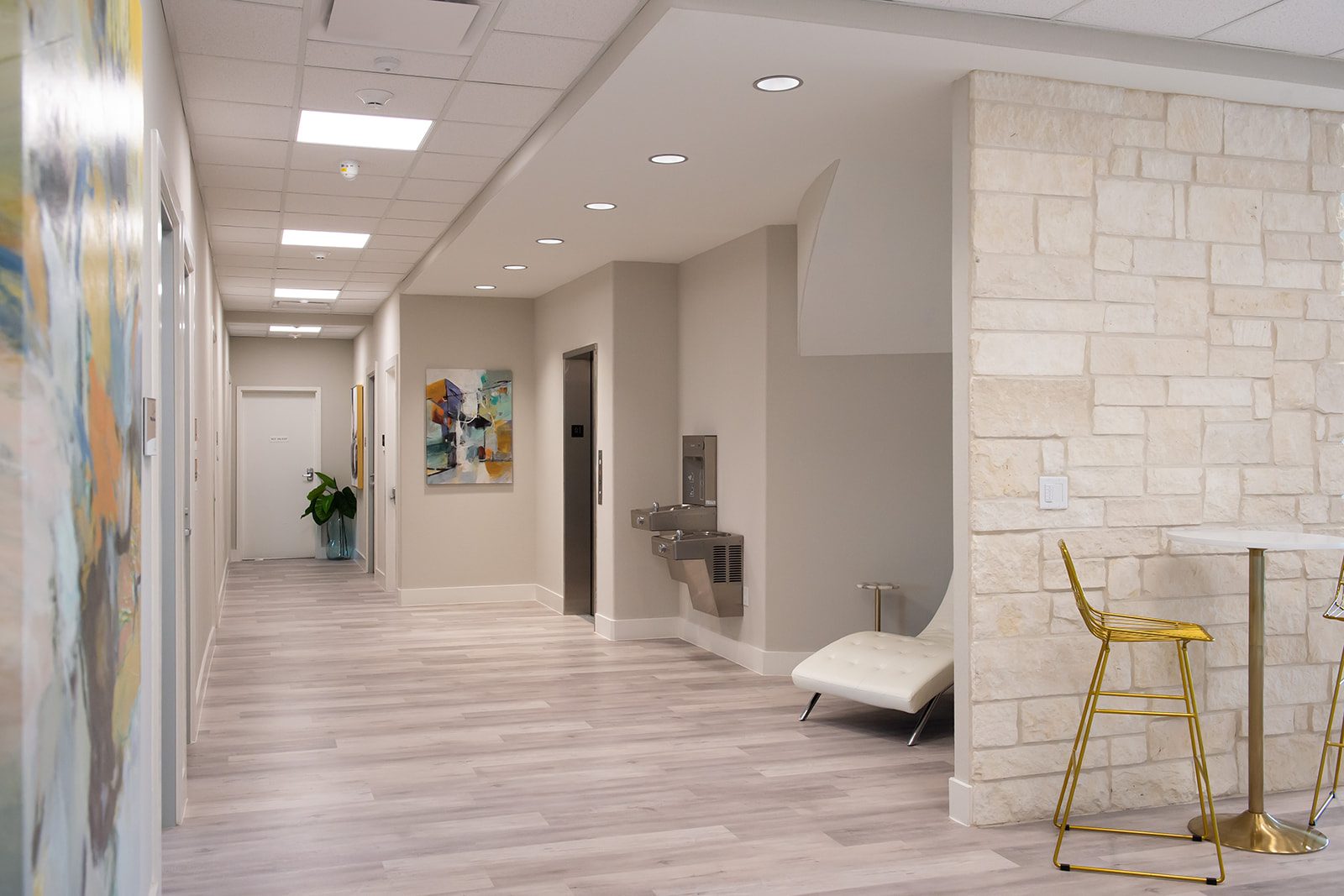 Bright Bellevana hallway with stone accent wall, original artwork, and white chaise